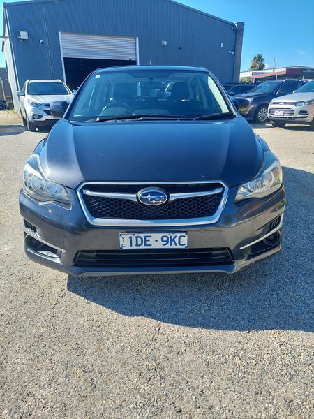 A dark gray Subaru Impreza sedan parked in front of a building on a sunny day. The car has a license plate