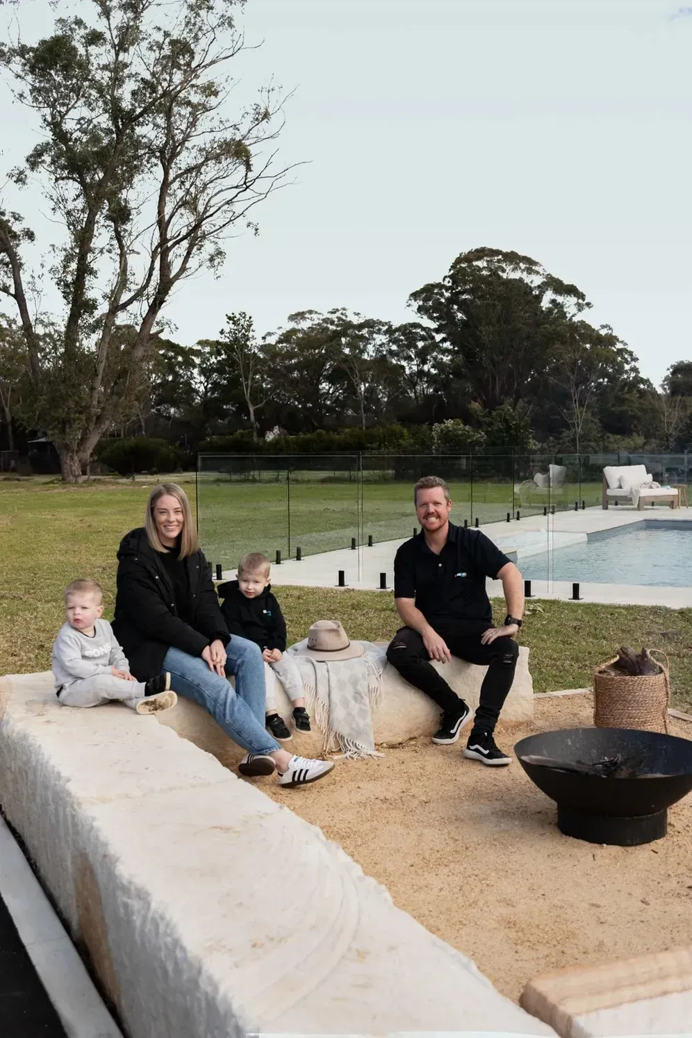 A Family Is Sitting on A Bench in Front of A Swimming Pool — Billabong Pool Co in Smeaton Grange, NSW