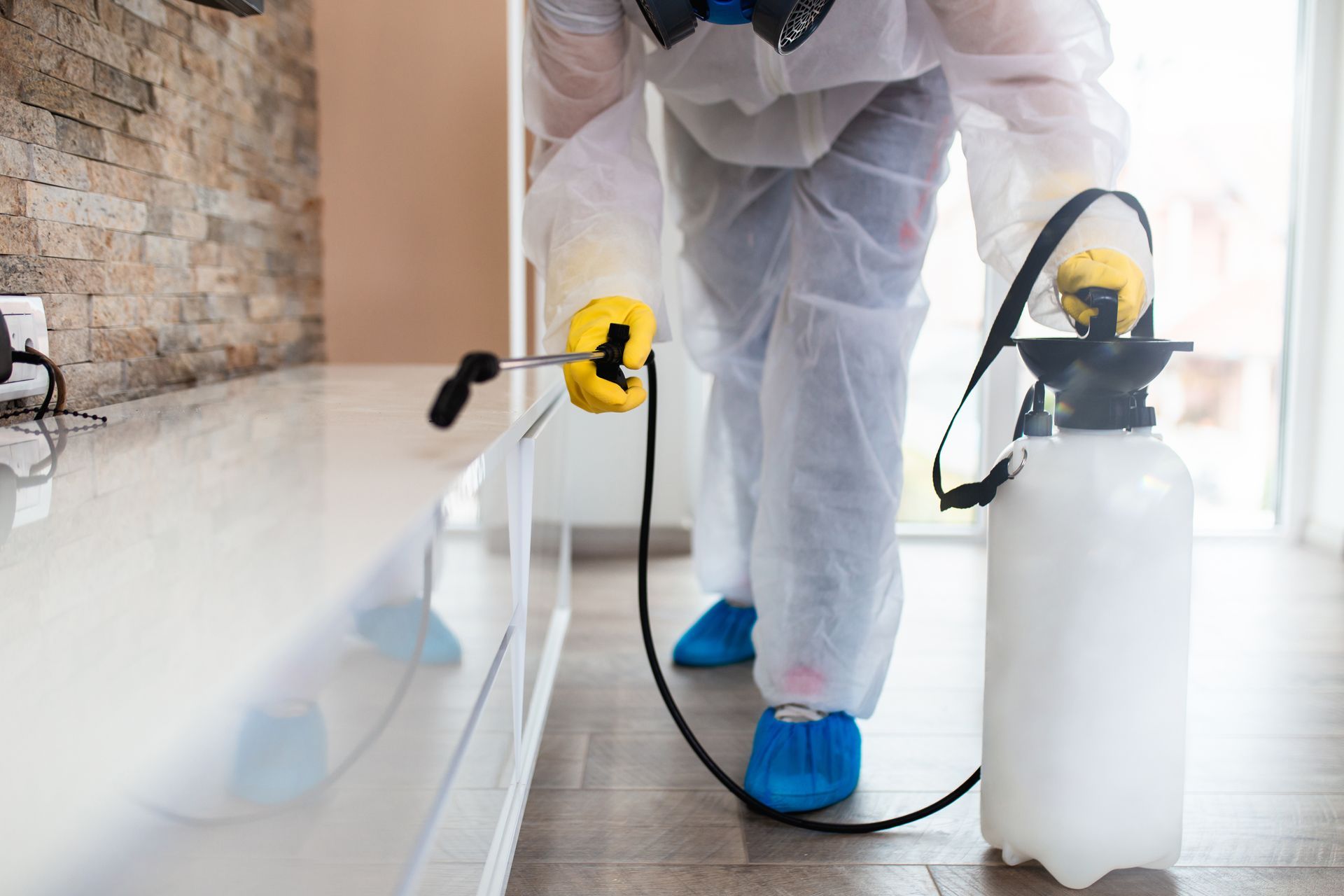 Technician in protective suit applying home pest control services treatment indoors.