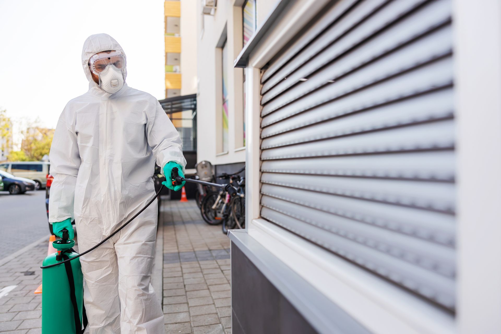 A man in a protective suit is spraying a building with a green sprayer.