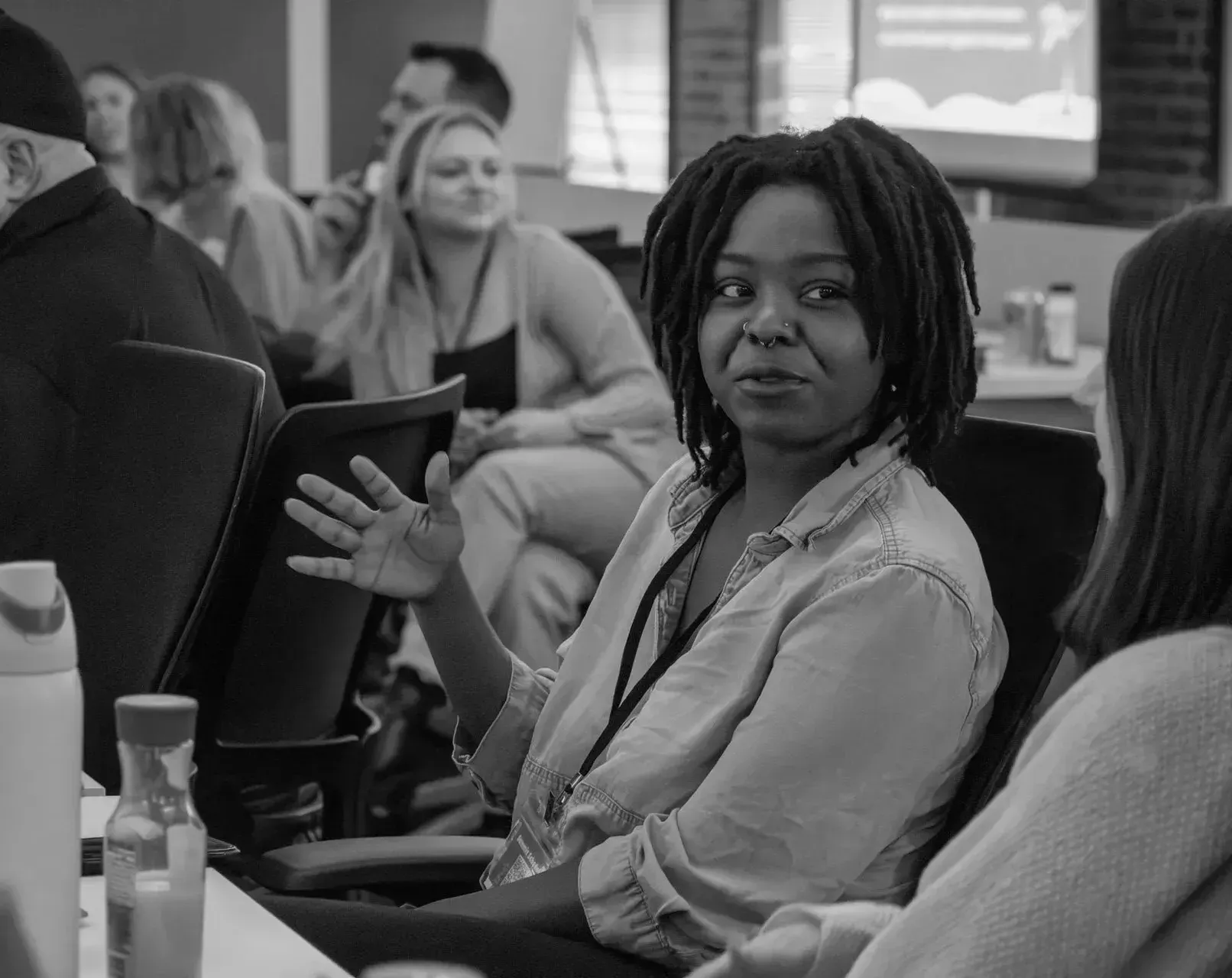 Black woman with dreadlocks gesturing during a meeting, speaking to another person.