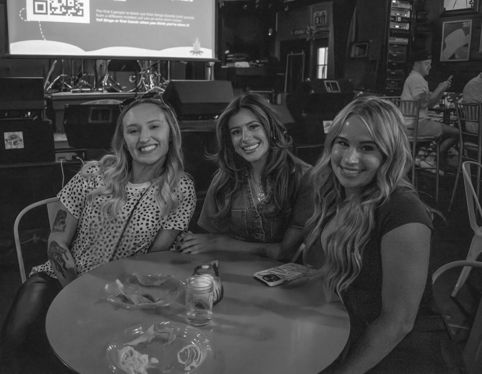Three smiling women at a table in a dimly lit bar.
