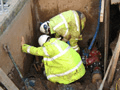 Two construction workers are working on a pipe in a trench.