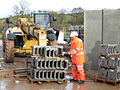 A man is standing next to a stack of bricks in front of a bulldozer.