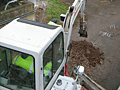 A man is driving a white excavator on a dirt road.