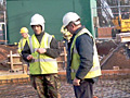 Two construction workers are standing next to each other on a construction site.