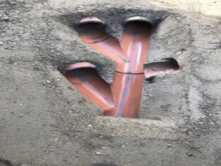 Davis Groundworks | Three red pipes are laying in the dirt in a hole.