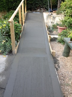 A concrete walkway with a wooden railing in a garden