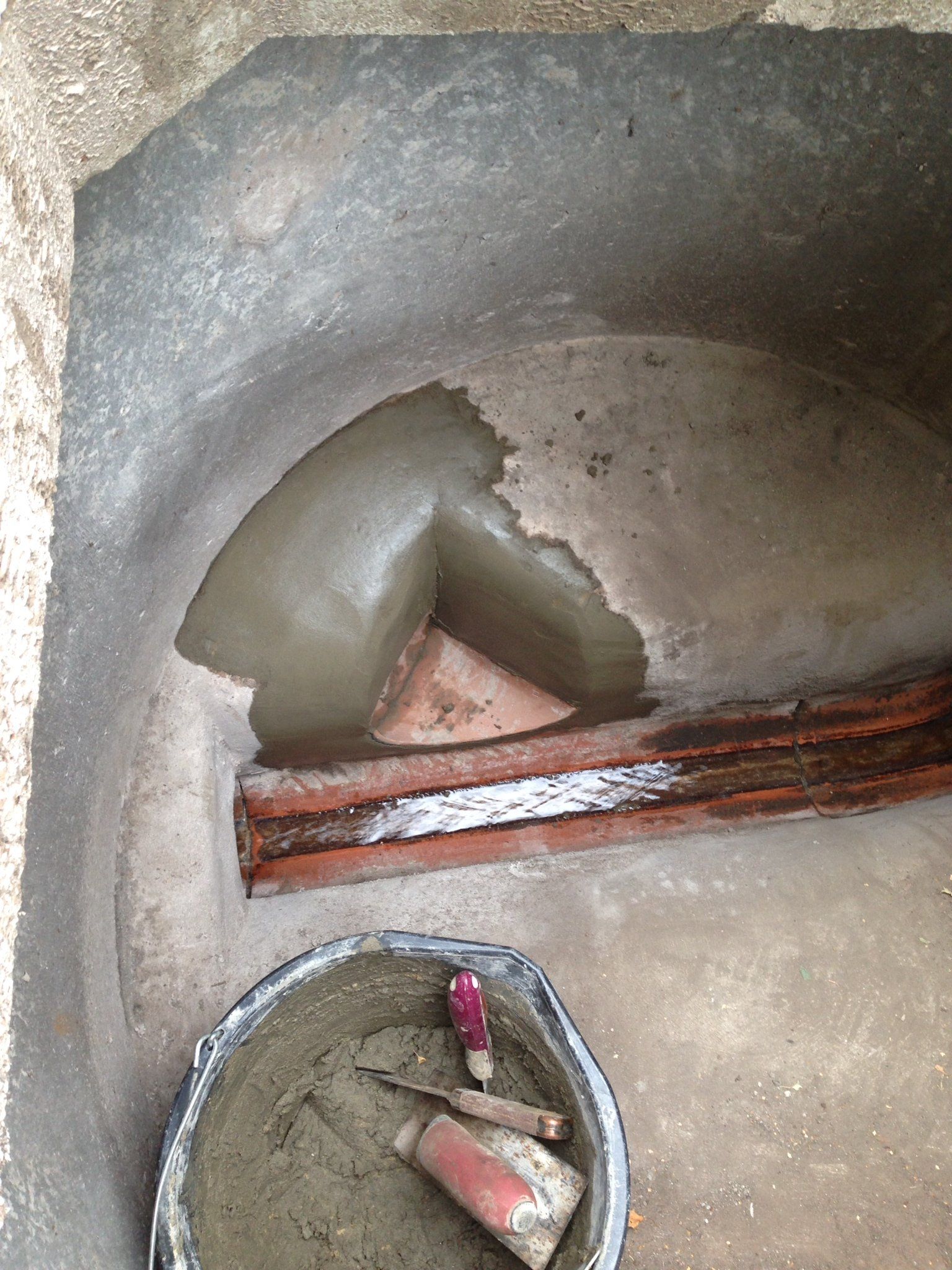 A bucket of cement is sitting next to a brick wall.