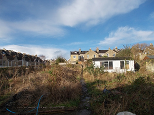 A house is sitting in the middle of a field in front of a row of houses.