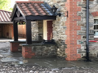 A cat is sitting on a porch next to a brick building.