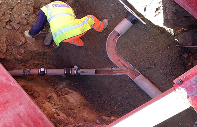 A man in a yellow vest is working on a pipe