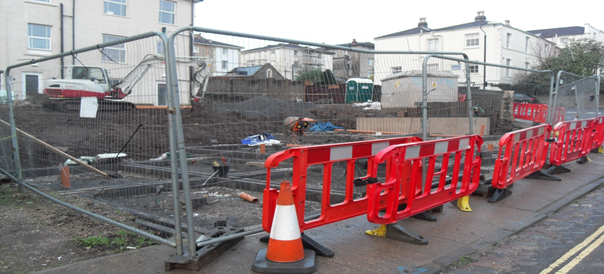 A construction site with a fence and cones on the side of the road.