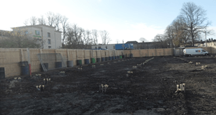 A construction site with a fence and a building in the background