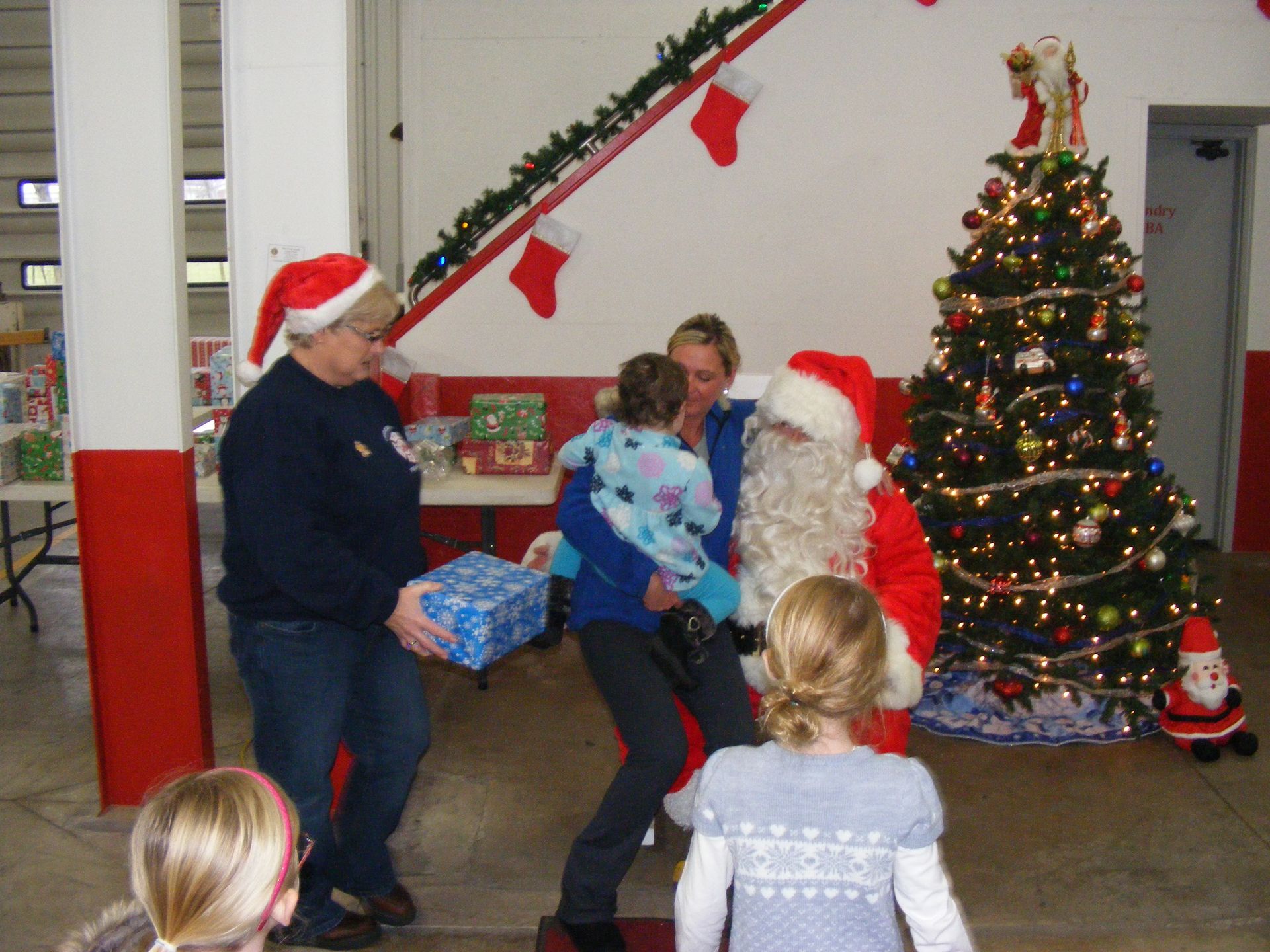 Santa with children, indoors; gifts, Christmas tree, red and white decor.