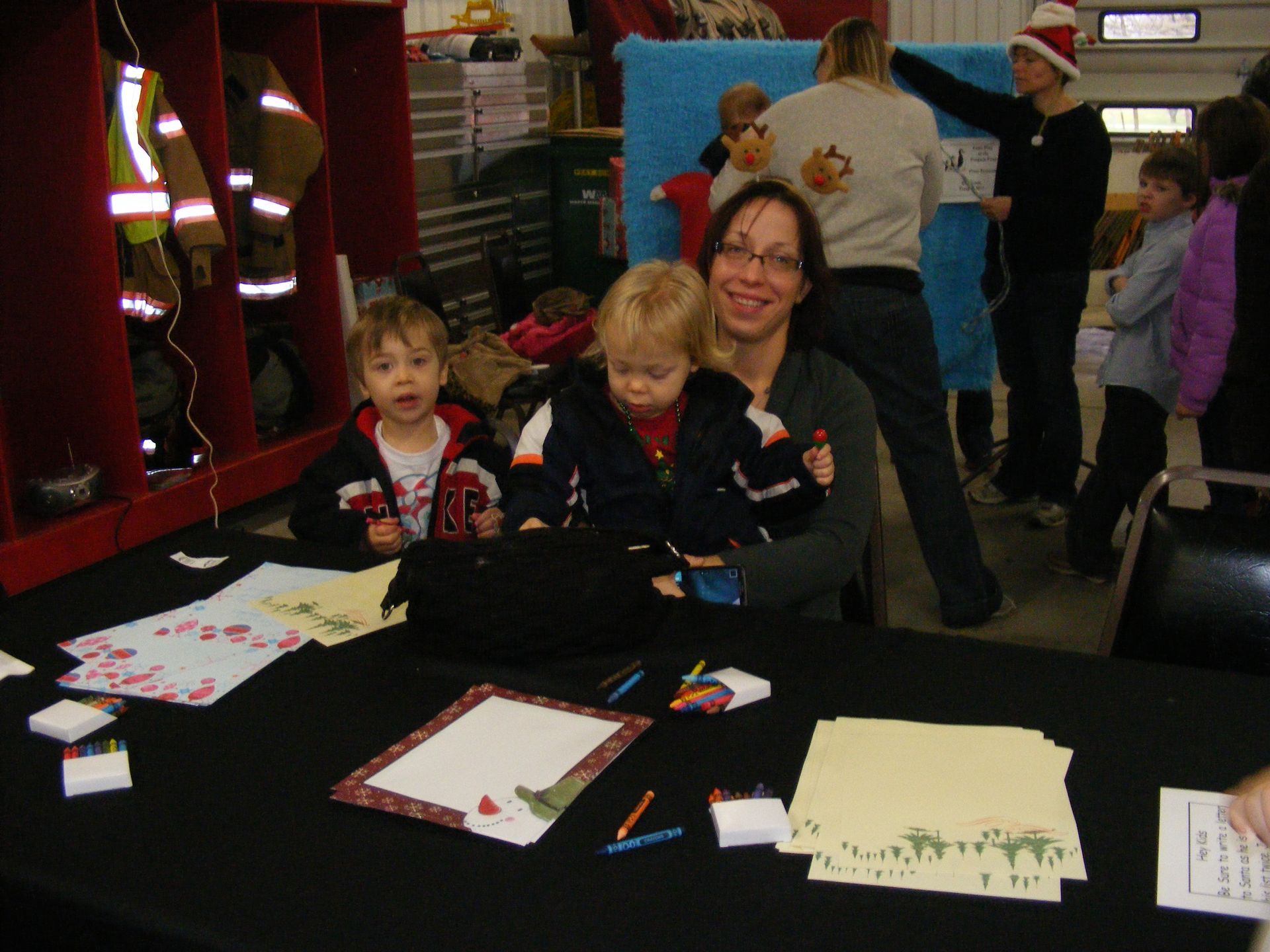 Woman and two children at a craft table, inside a building. They are smiling at the camera.