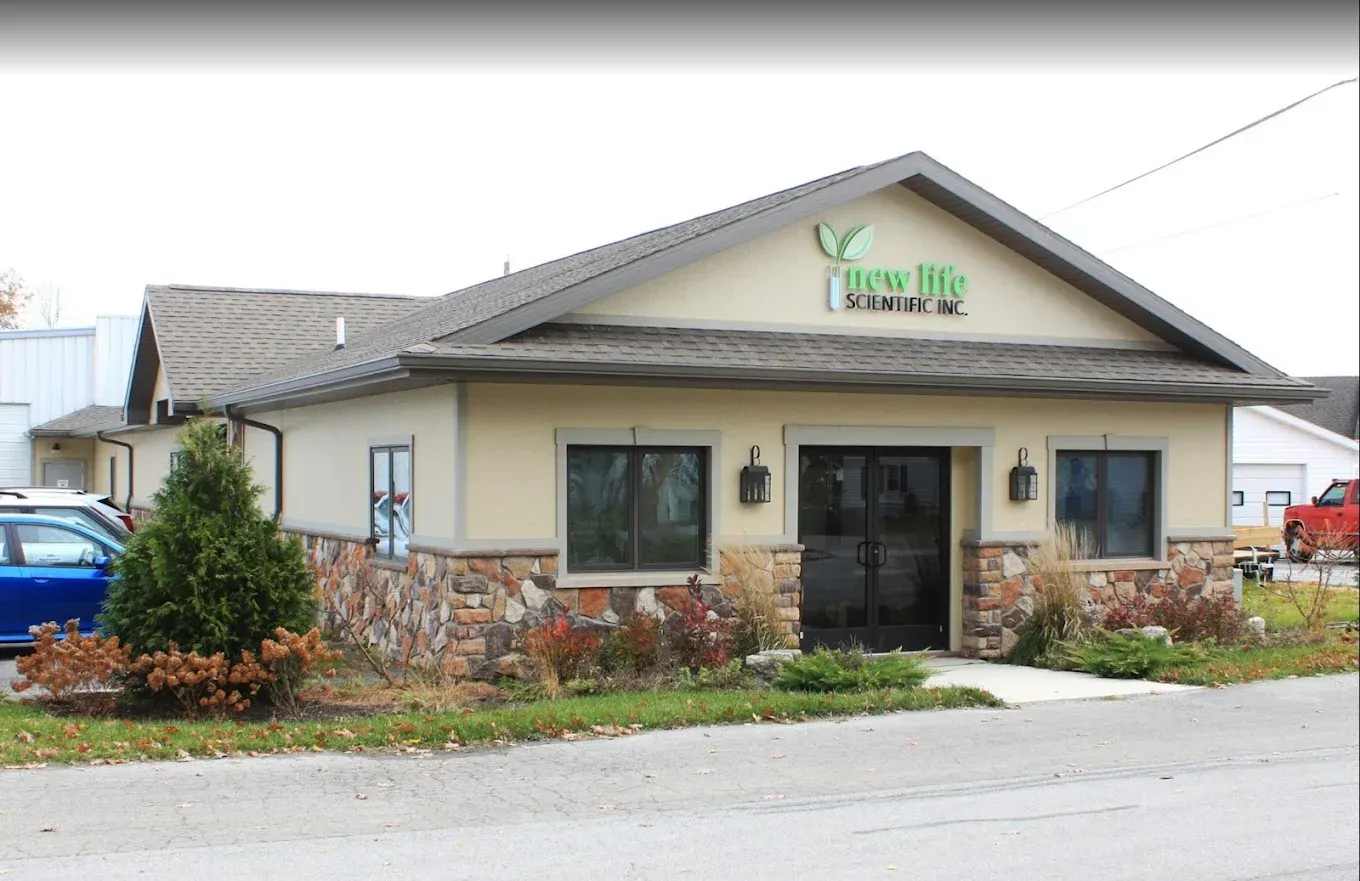 Tan building with stone accents and green sign; grassy area in front, small evergreen tree to the left.