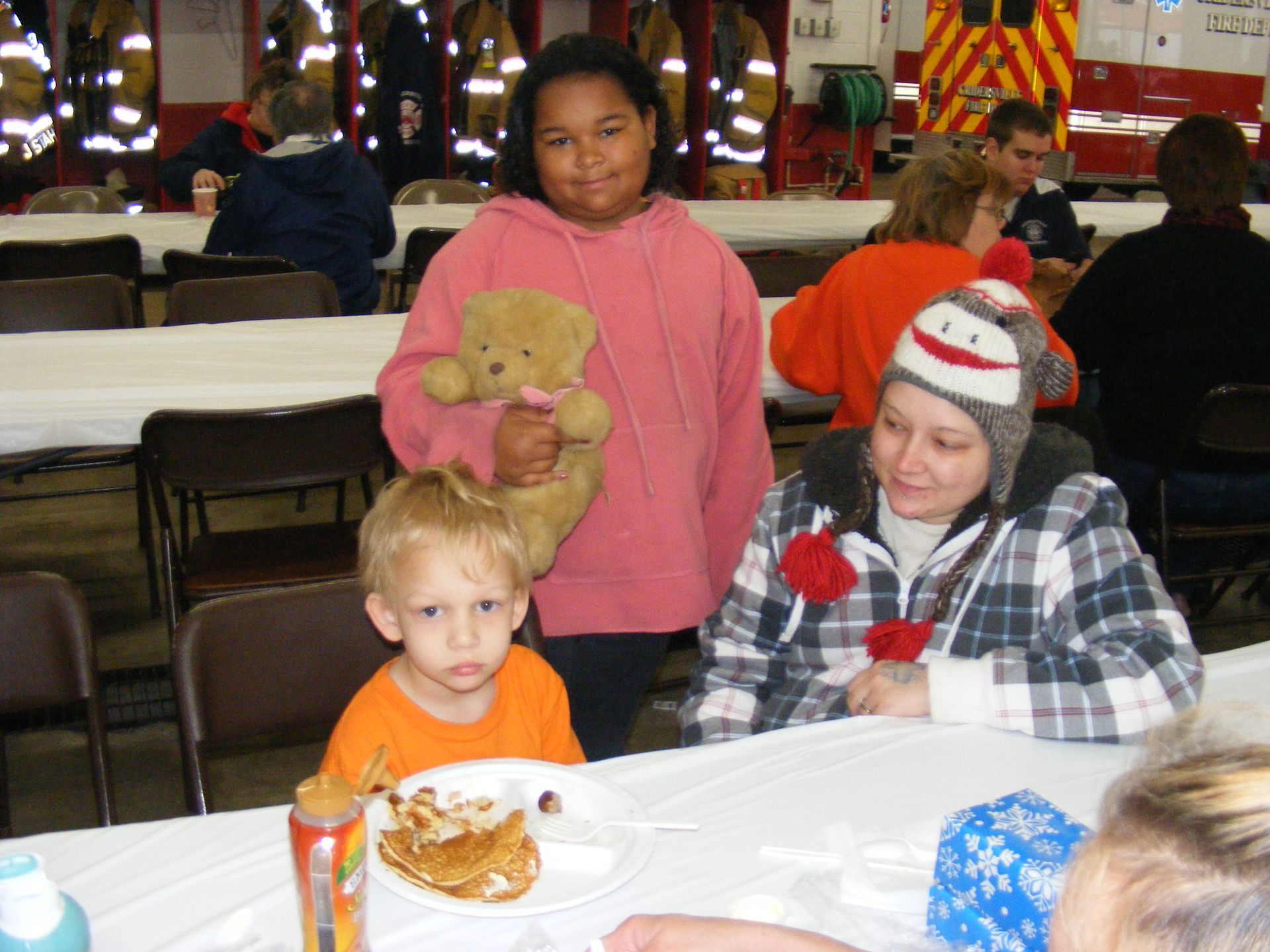 A young girl, boy, and woman at a table, smiling at a community event.