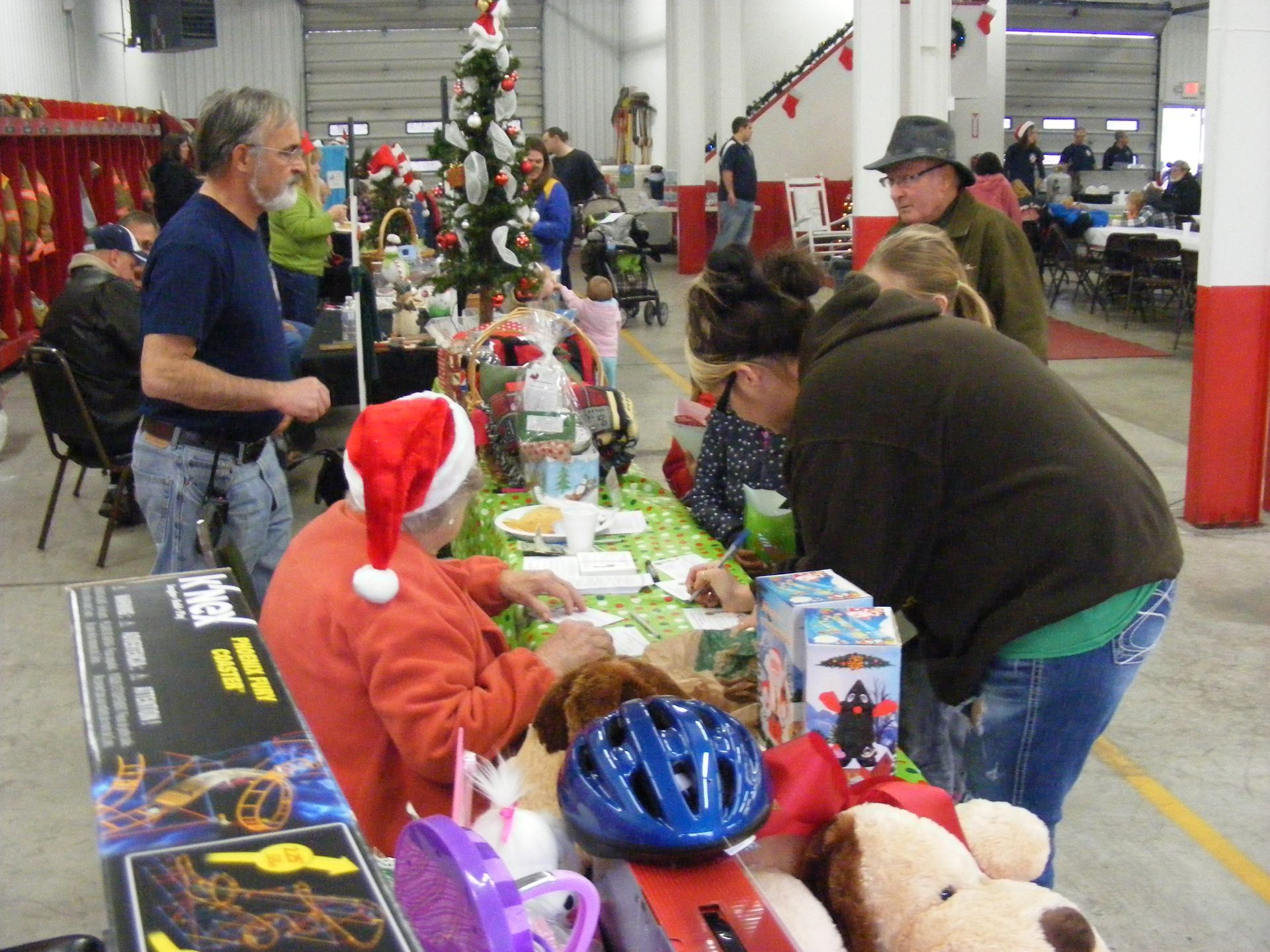 People browsing toys at a Christmas event in a fire station. A Santa hat is visible.