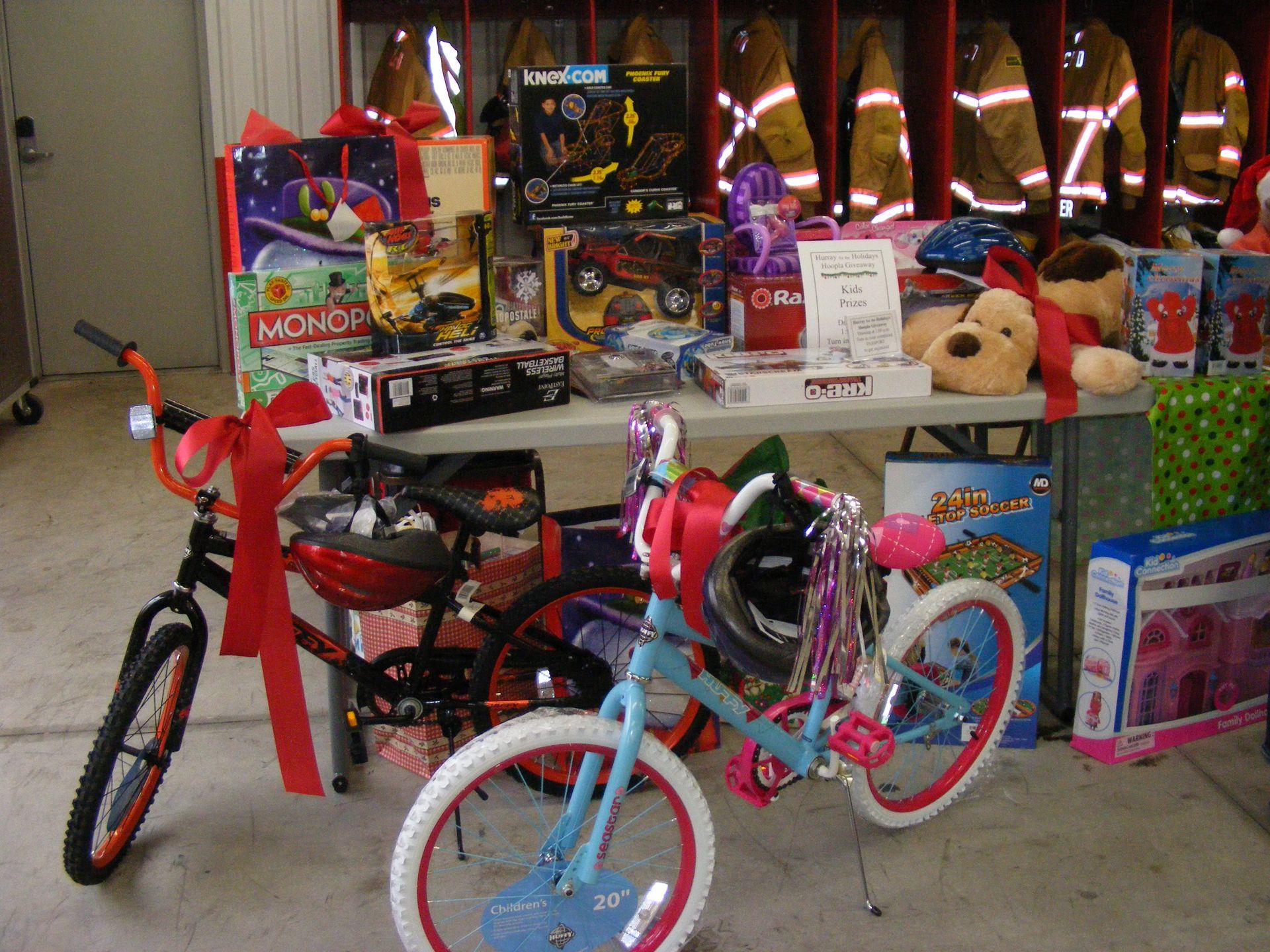 Gifts, toys, and bikes on a table, possibly for a holiday donation. Firefighter jackets are in the background.