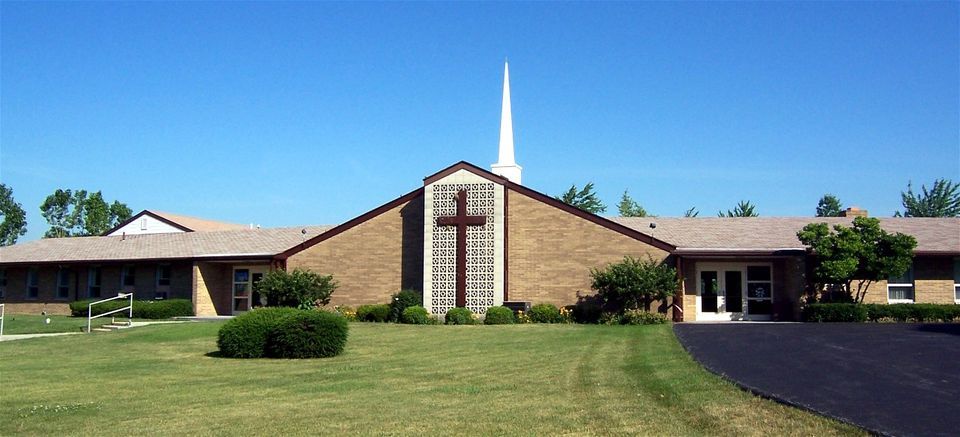 Church with cross on front facade; green lawn; blue sky.