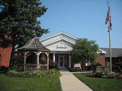 Library building with gazebo, walkway, flag, and manicured lawn on a sunny day.