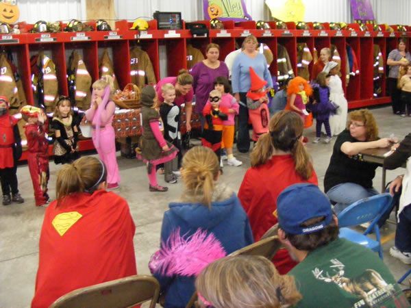 Kids in costumes at a fire station Halloween event; adults watching.