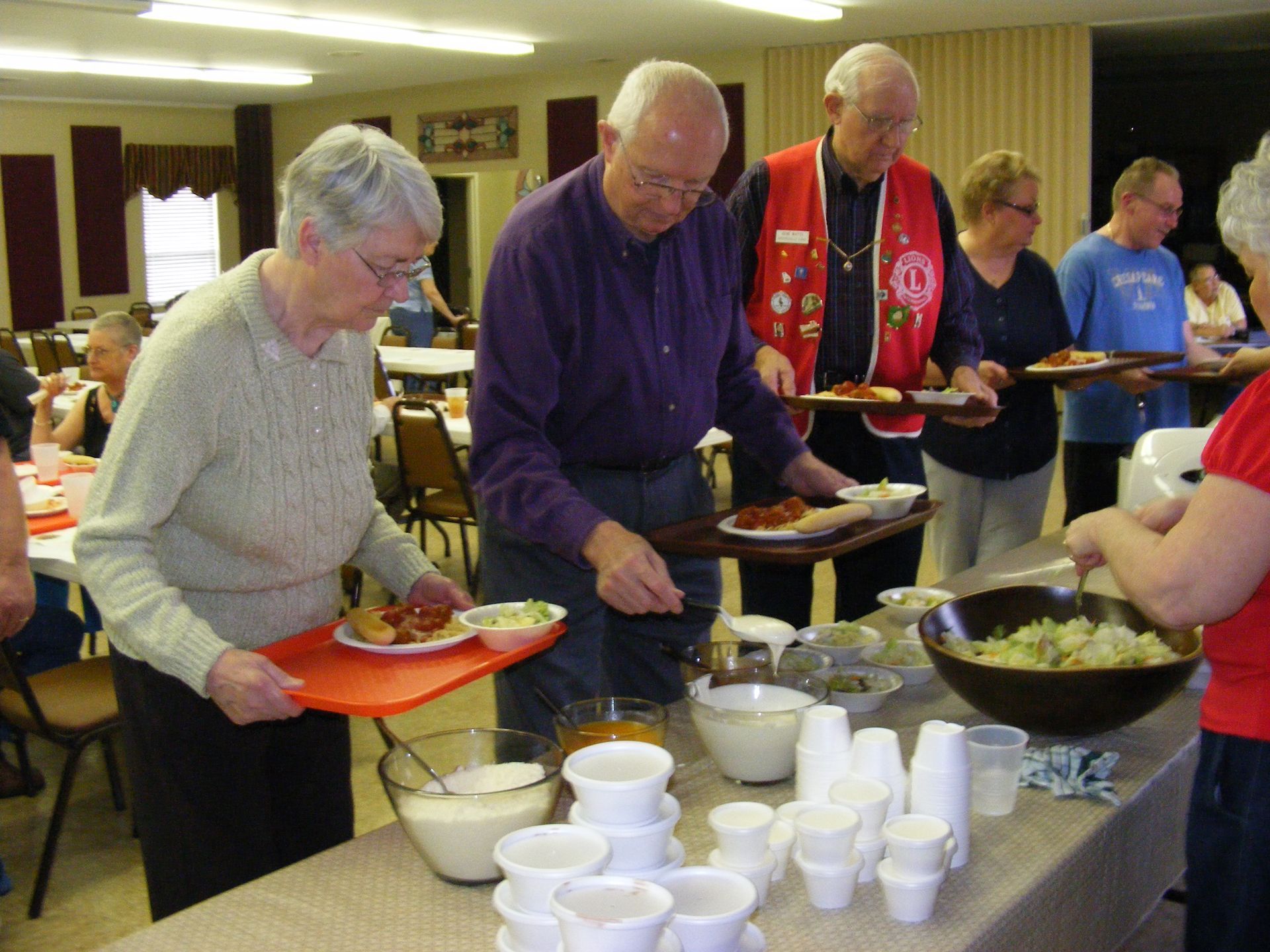 People serving themselves food from a buffet table at a community event.