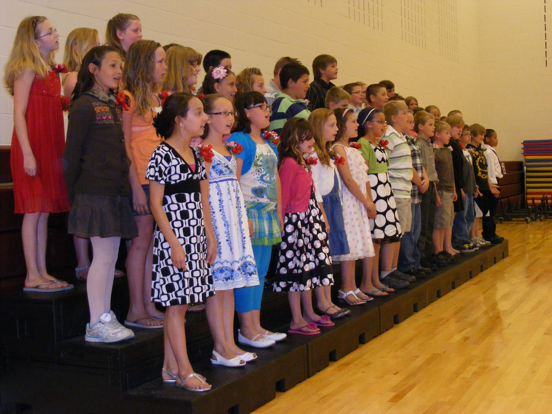 Children in colorful outfits standing on risers, likely performing.