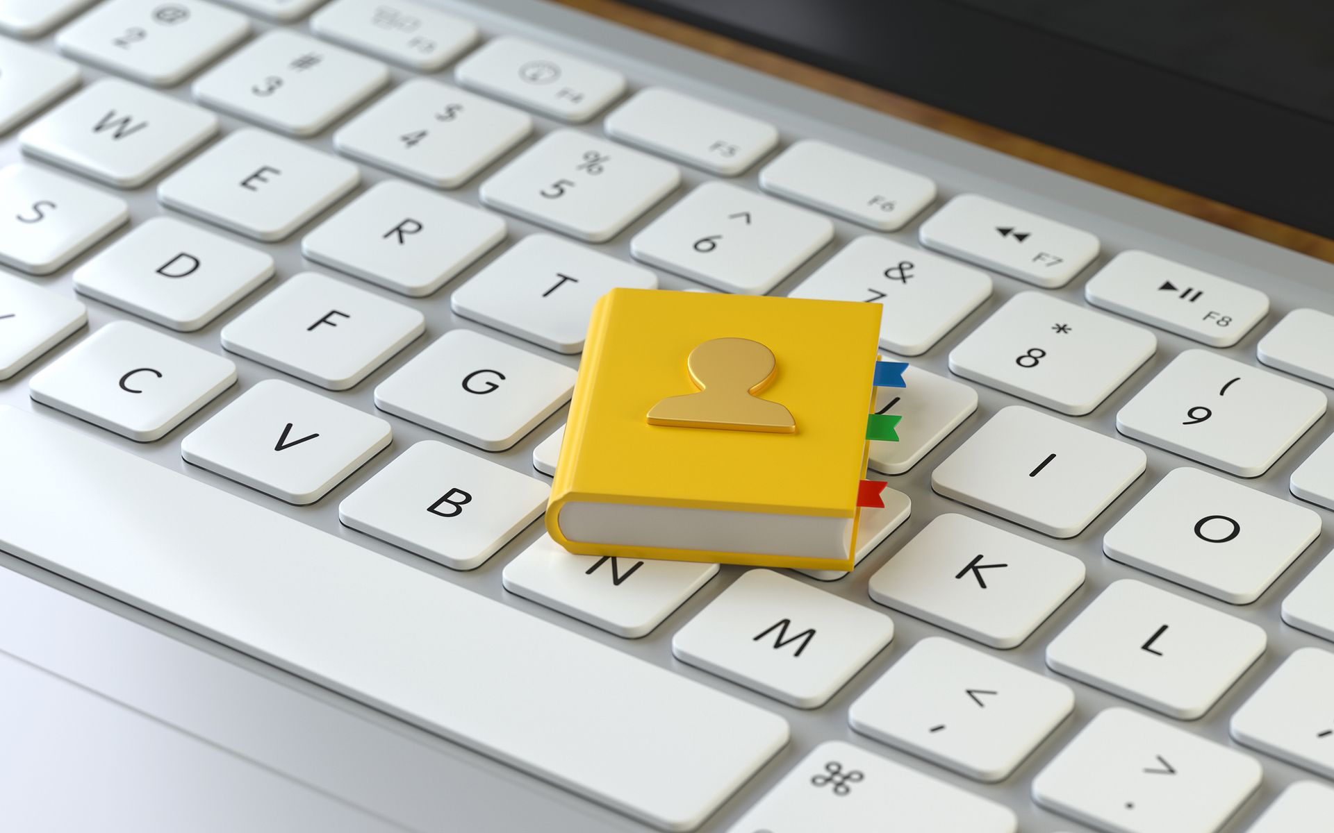Yellow address book on a white laptop keyboard, suggesting digital contact management.