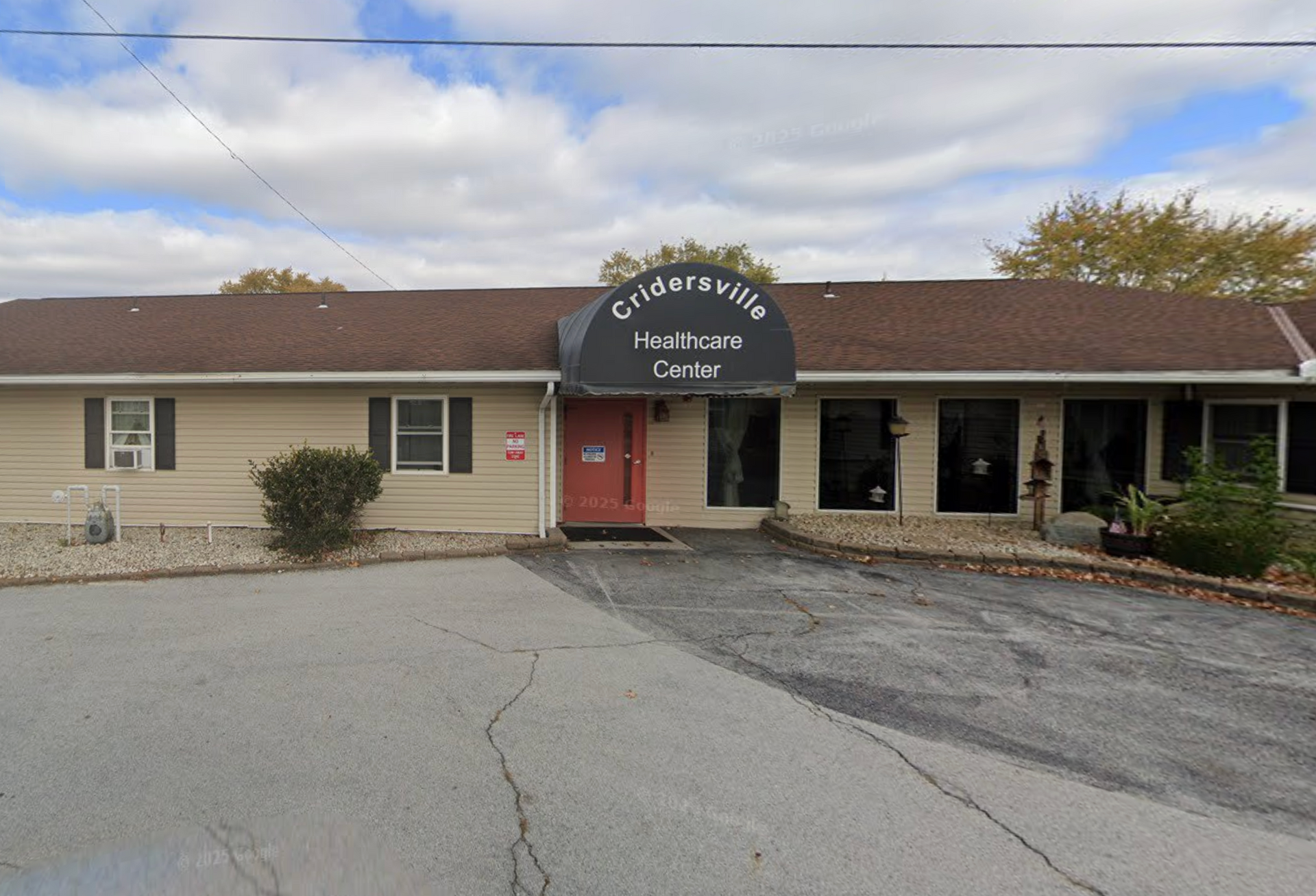 Exterior of Cridersville Healthcare Center; tan building, black awning over red door, cloudy sky.