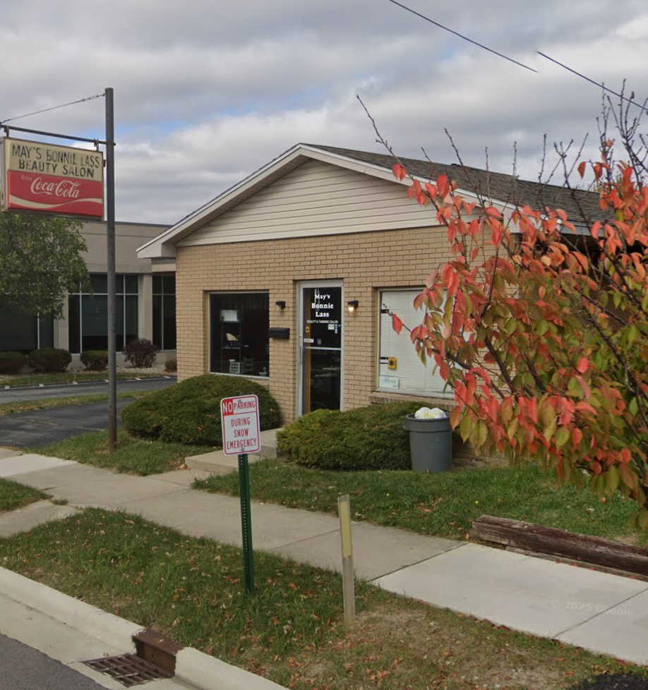 Exterior of a beauty salon with a Coca-Cola sign and red-leafed bush.
