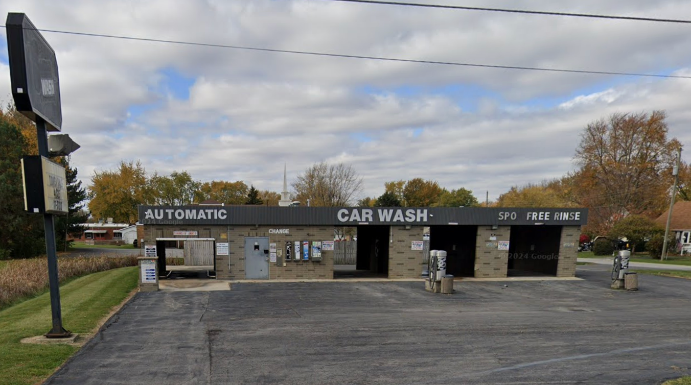 An automatic car wash with a black roof and sign, gray brick facade, and empty bays.