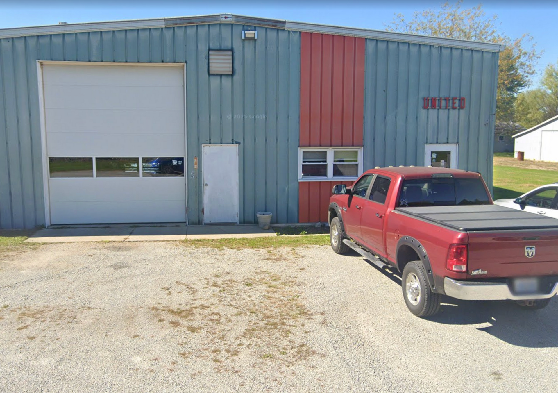 Red pickup truck parked in front of a blue and red industrial building with a garage door and a white door.