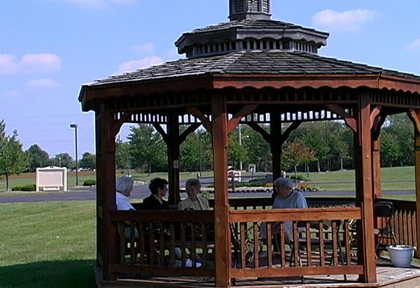 Four people sit in a brown gazebo, outdoors on a sunny day.