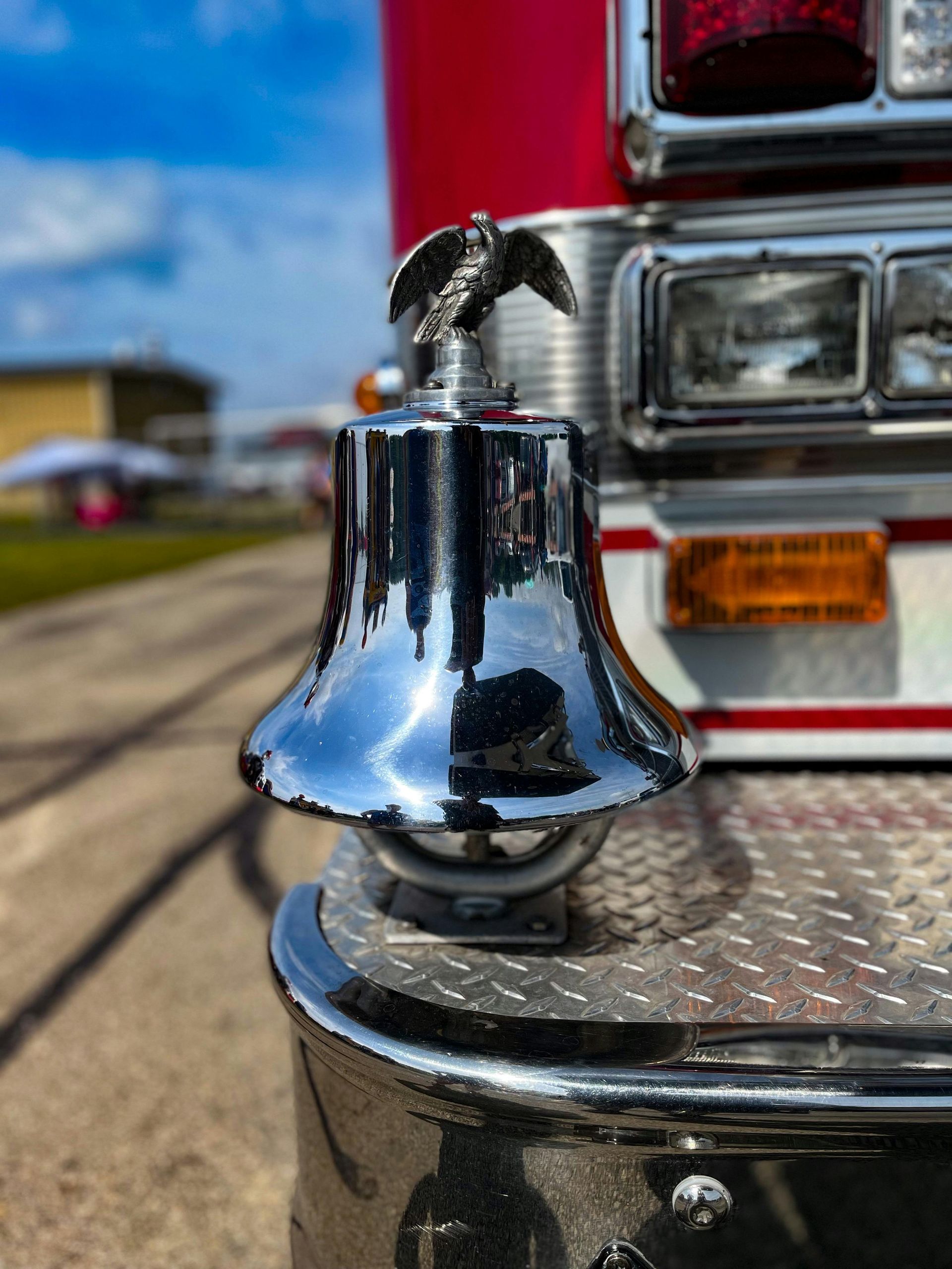 Shiny chrome fire truck bell with eagle emblem, mounted on the front bumper.