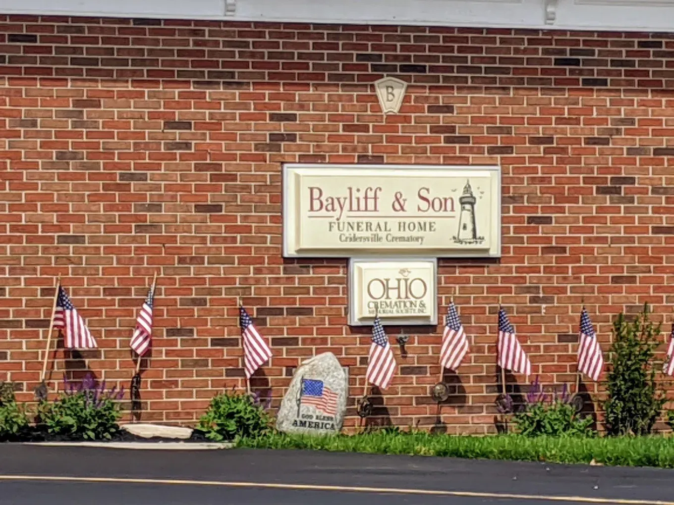 Bayliff & Son Funeral Home sign on a brick building with American flags and a stone.