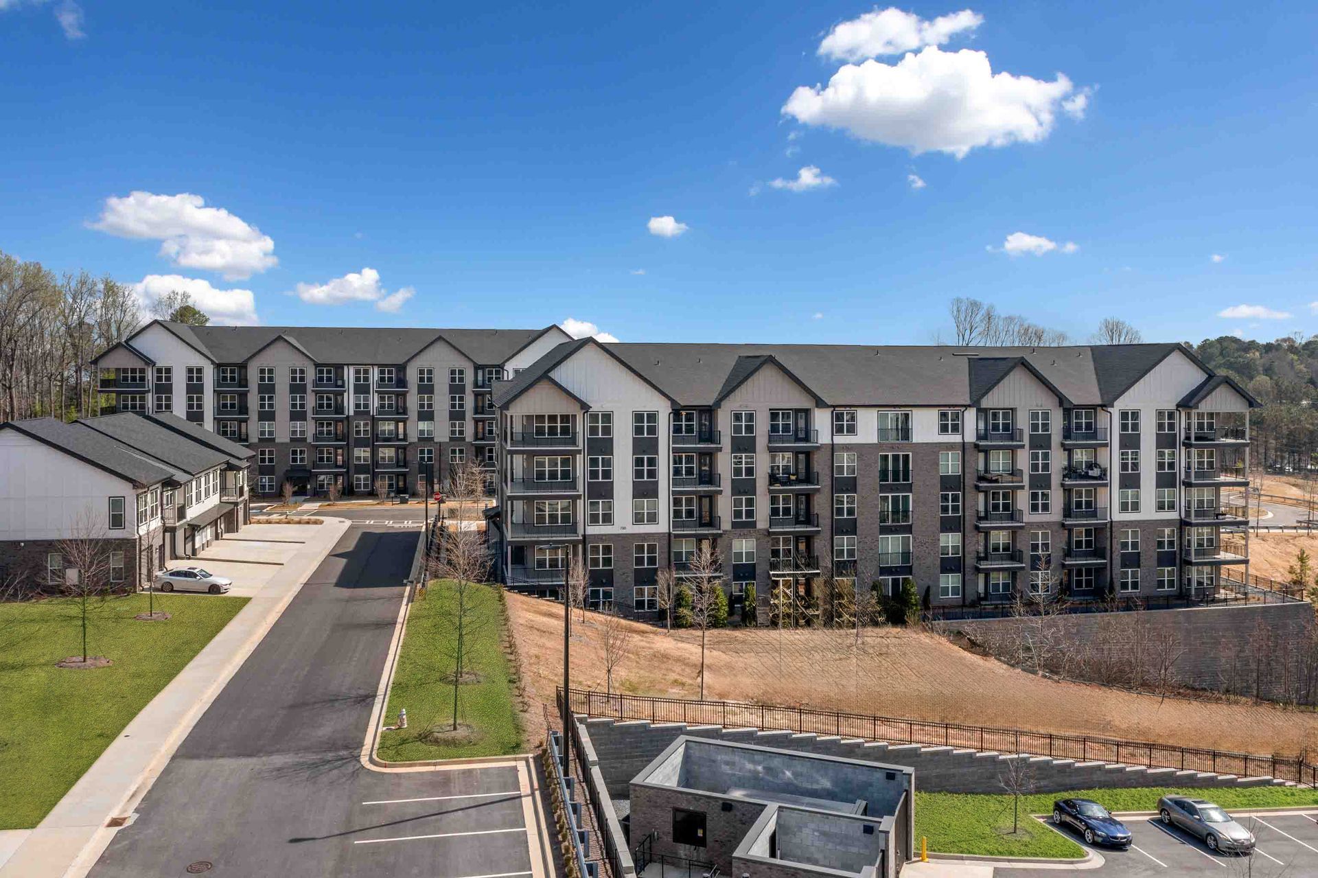 Multi-story apartment buildings with balconies, asphalt road, blue sky, and clouds.