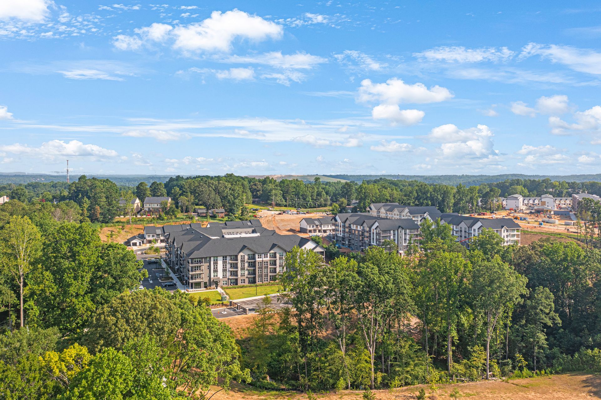 Aerial view of apartment complex amidst trees under a blue sky with scattered clouds.