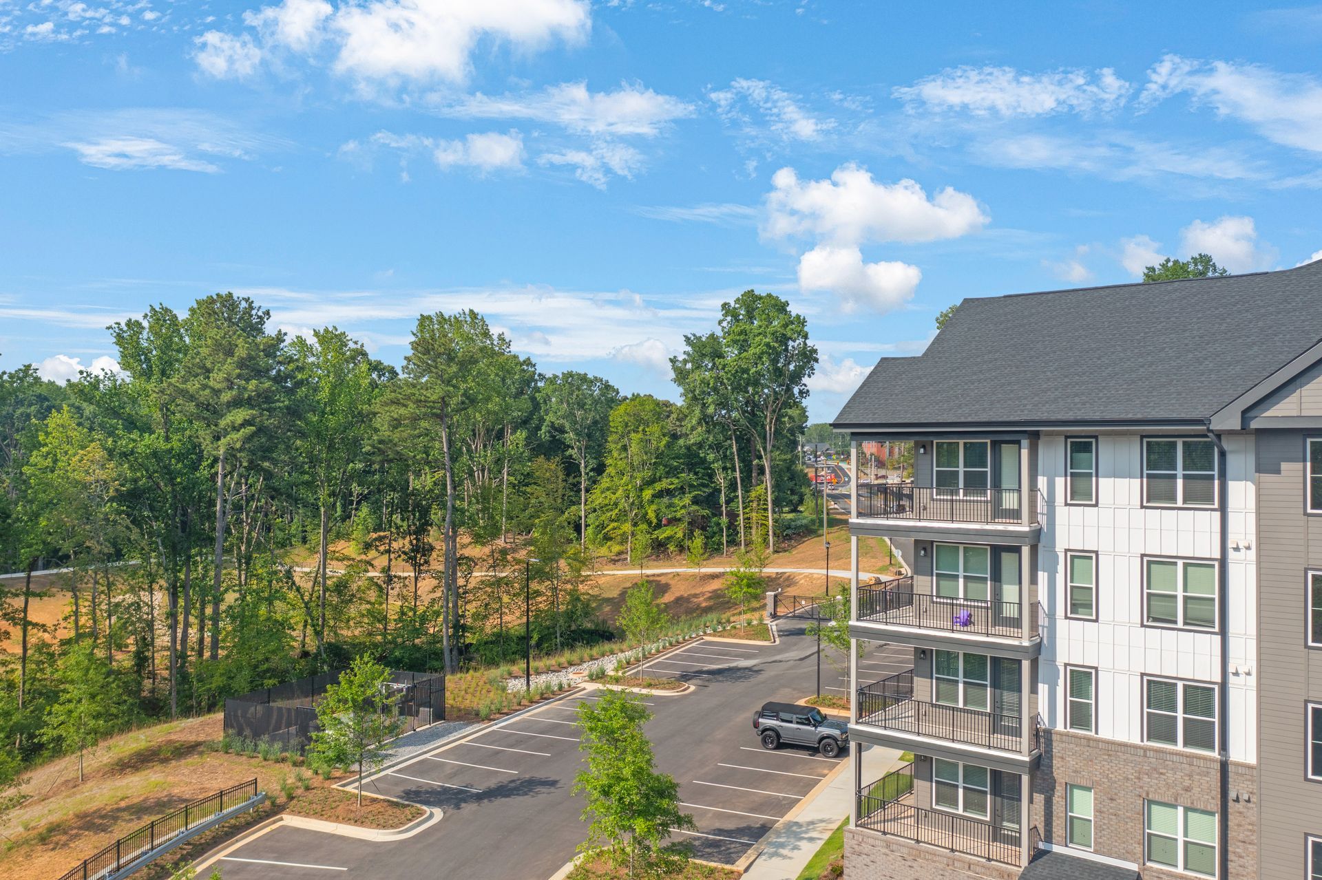 Apartment building exterior, parked car, trees, and blue sky.