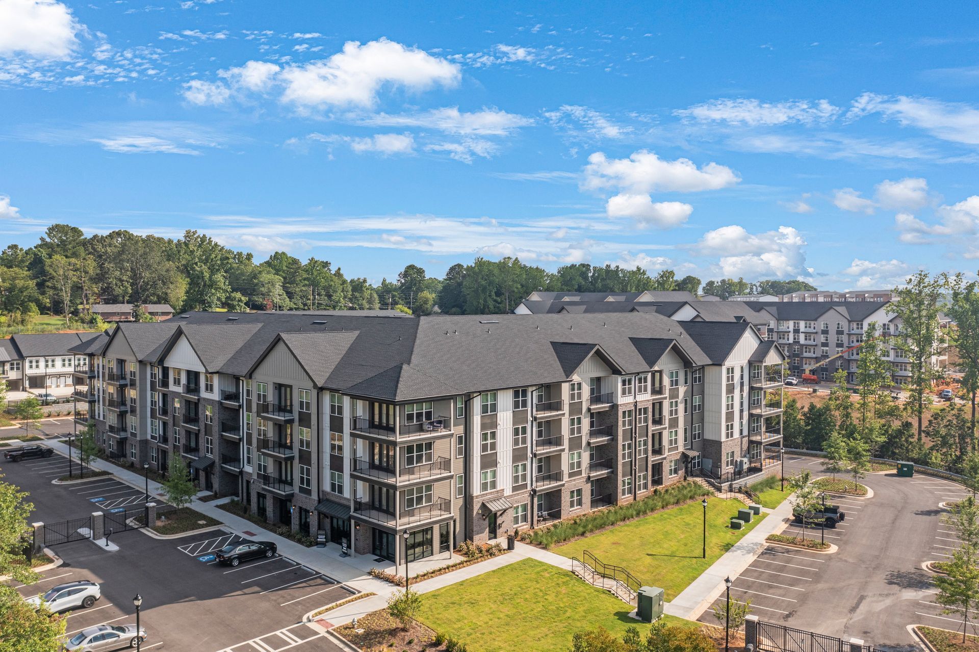 Multi-story apartment building with dark roof, gray and stone facade, under blue sky.