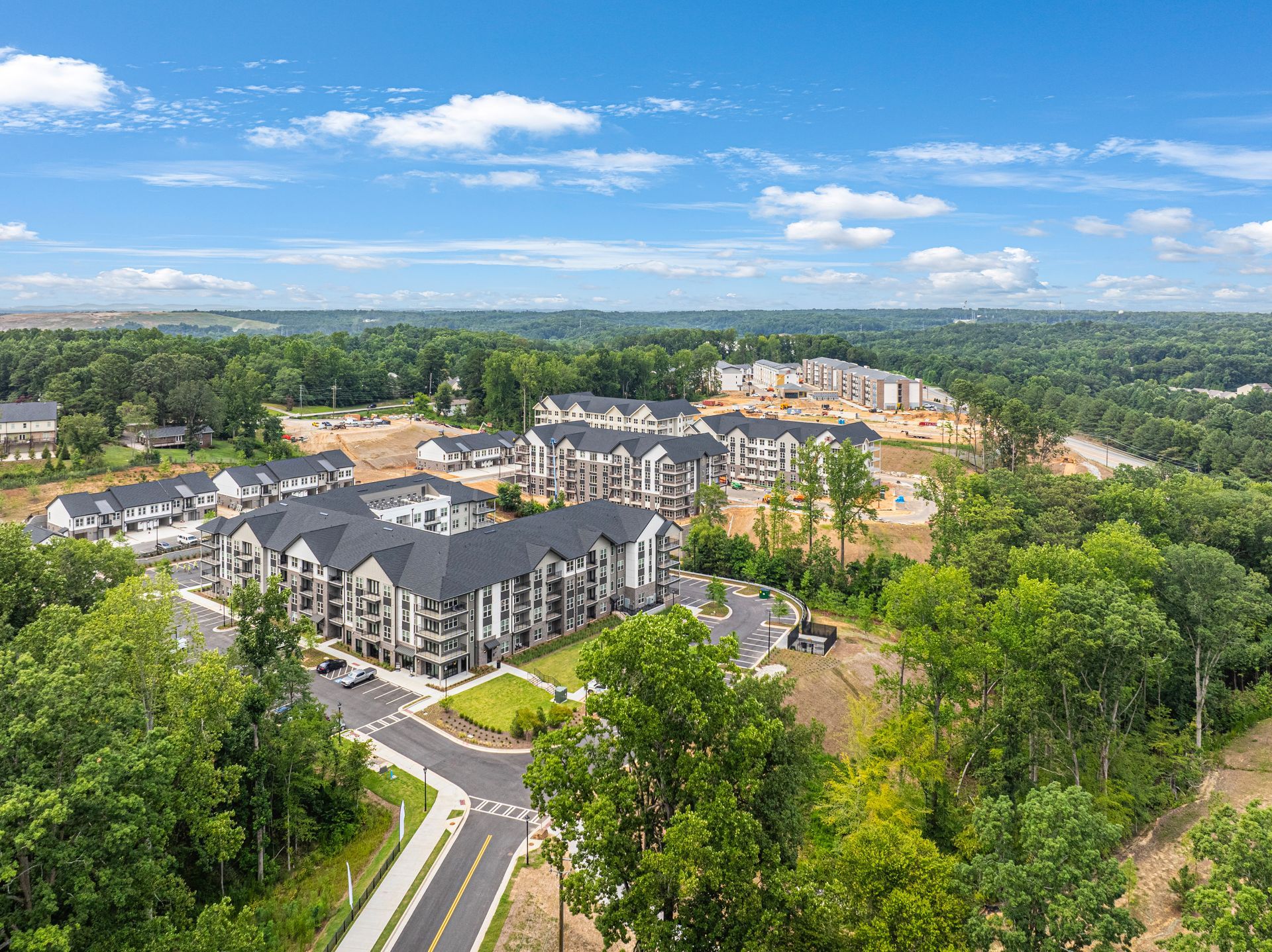 Aerial view of apartment complex with dark roofs, surrounded by trees and construction.