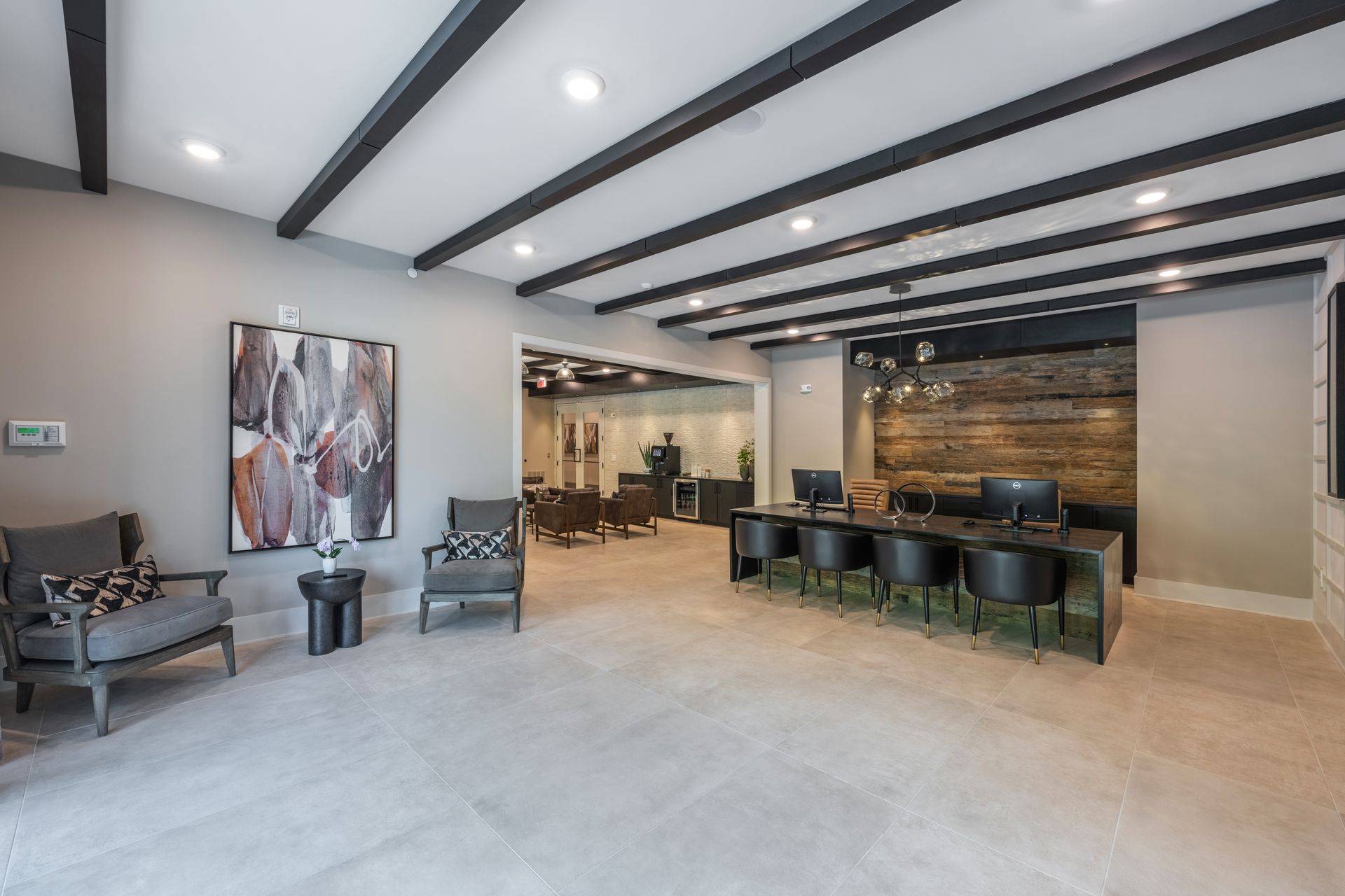 Modern reception area with gray walls, black ceiling beams, seating, and a reception desk.