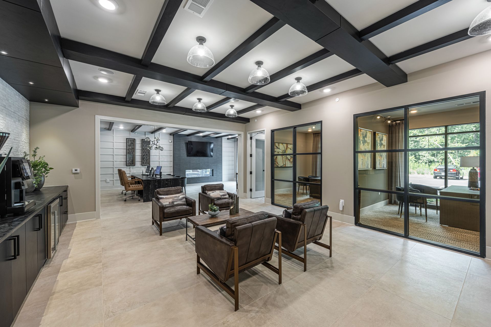 Lounge area with seating, glass doors, and black ceiling beams. Beige walls, stone floor, and pendant lights.