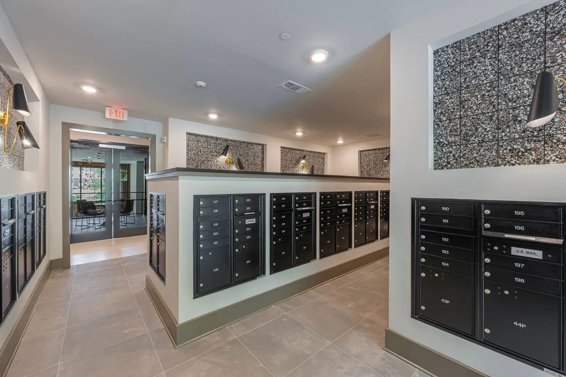 A hallway with lots of mailboxes and a red exit sign