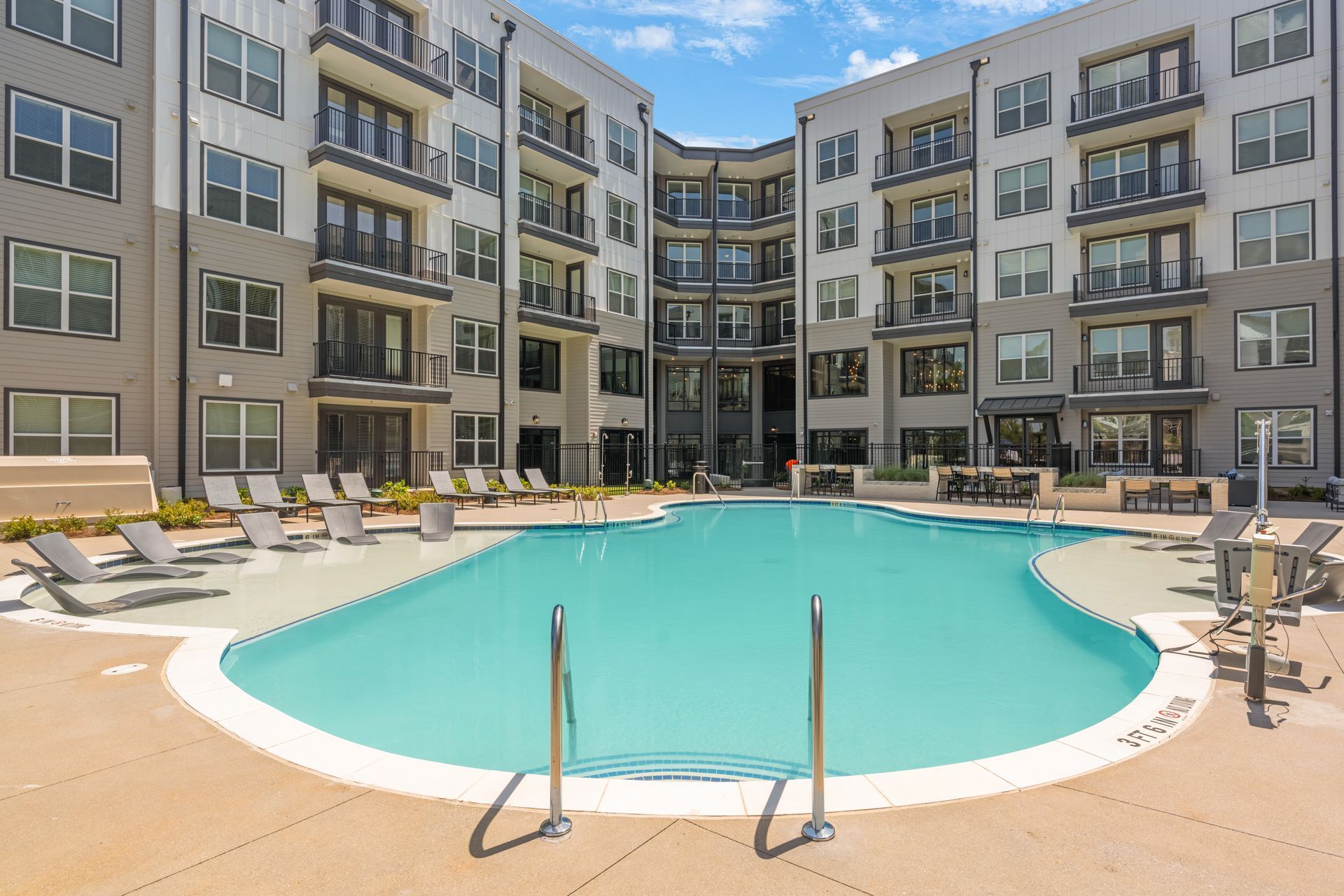Pool in courtyard of modern apartment building with lounge chairs.