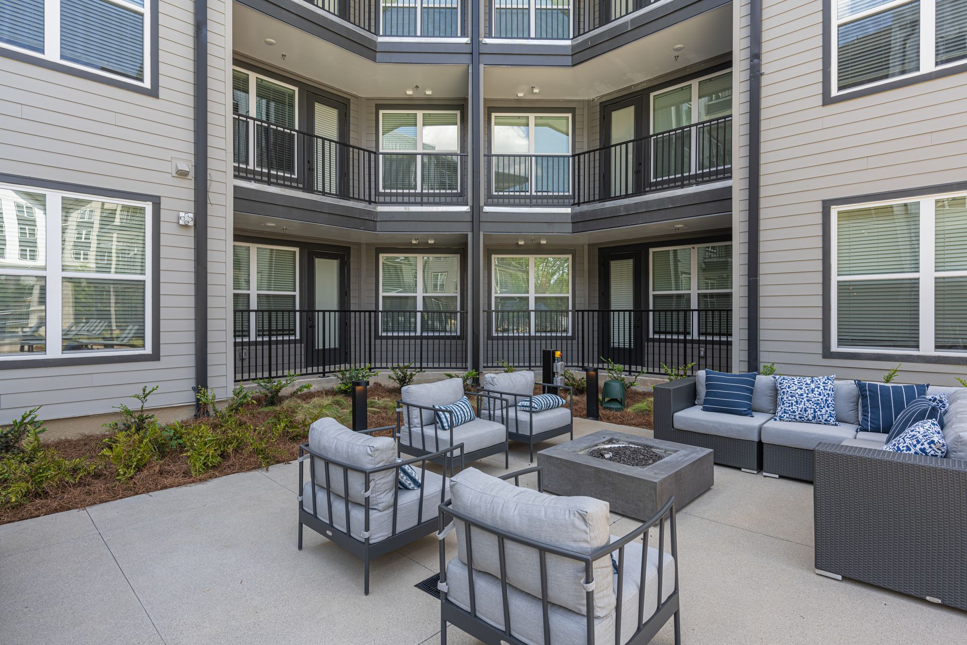Outdoor seating area with gray furniture, fire pit, and building with balconies.
