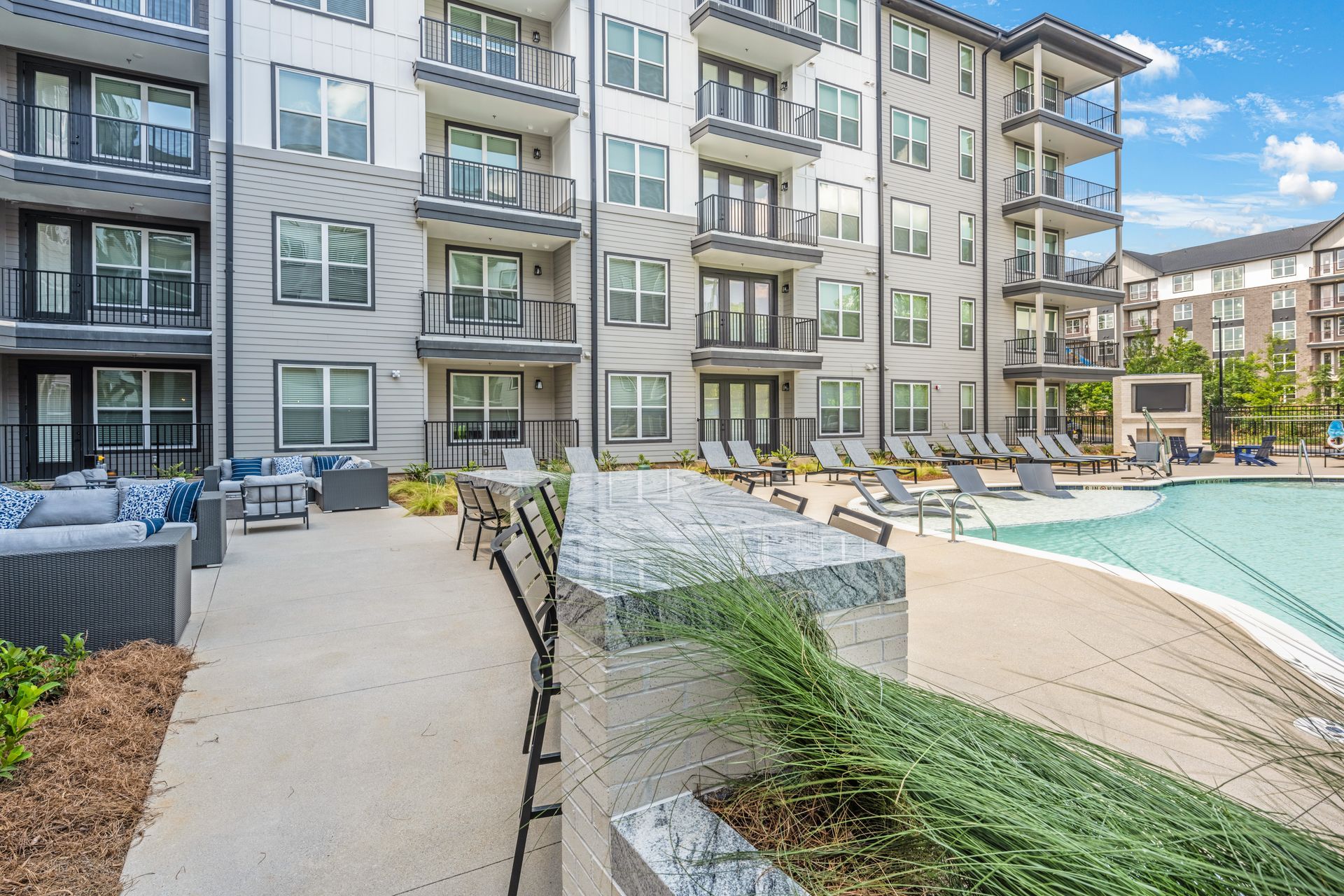Apartment complex with a pool and patio seating. Gray and white building with balconies.