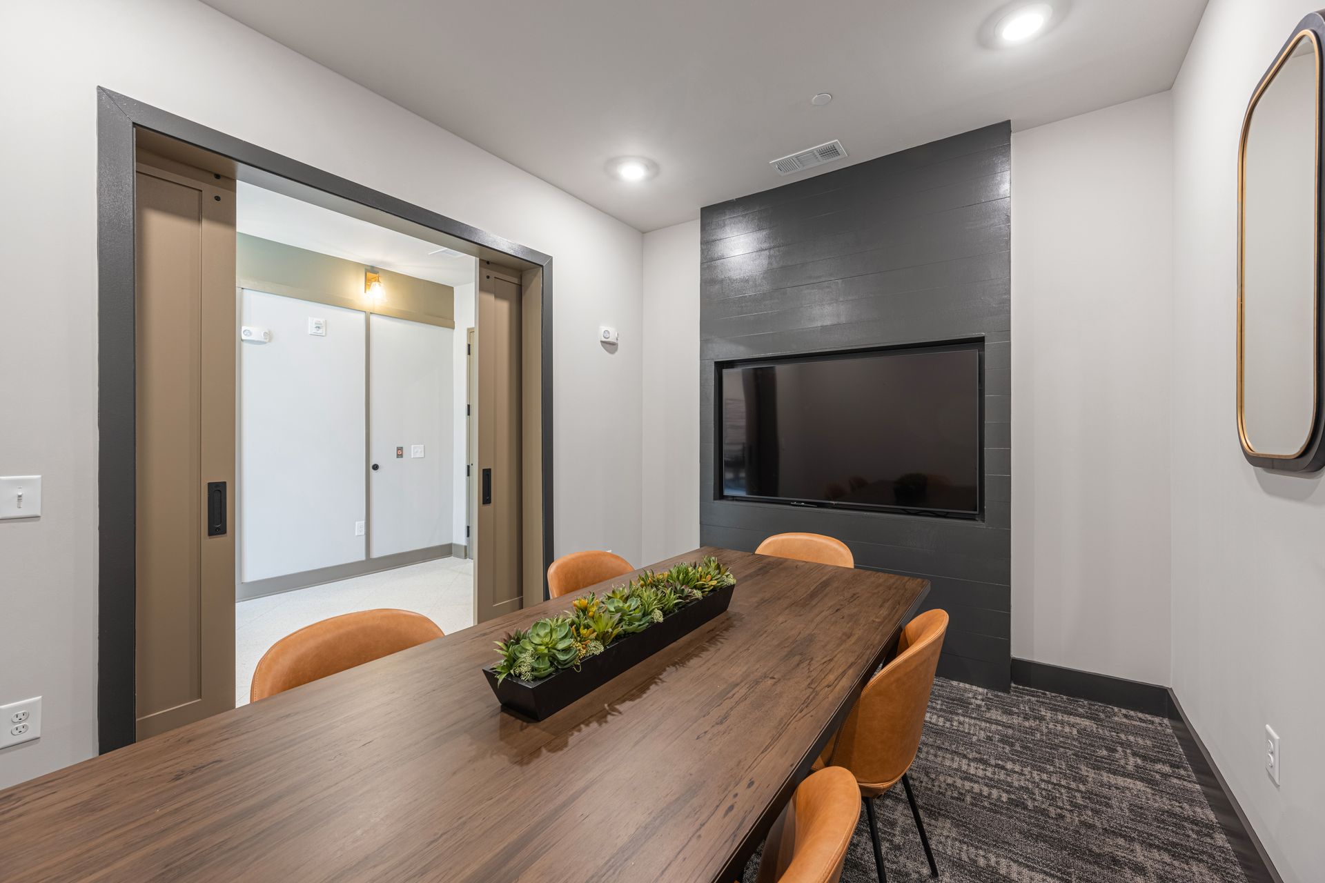 Conference room with wood table, orange chairs, TV, and open door to hallway.