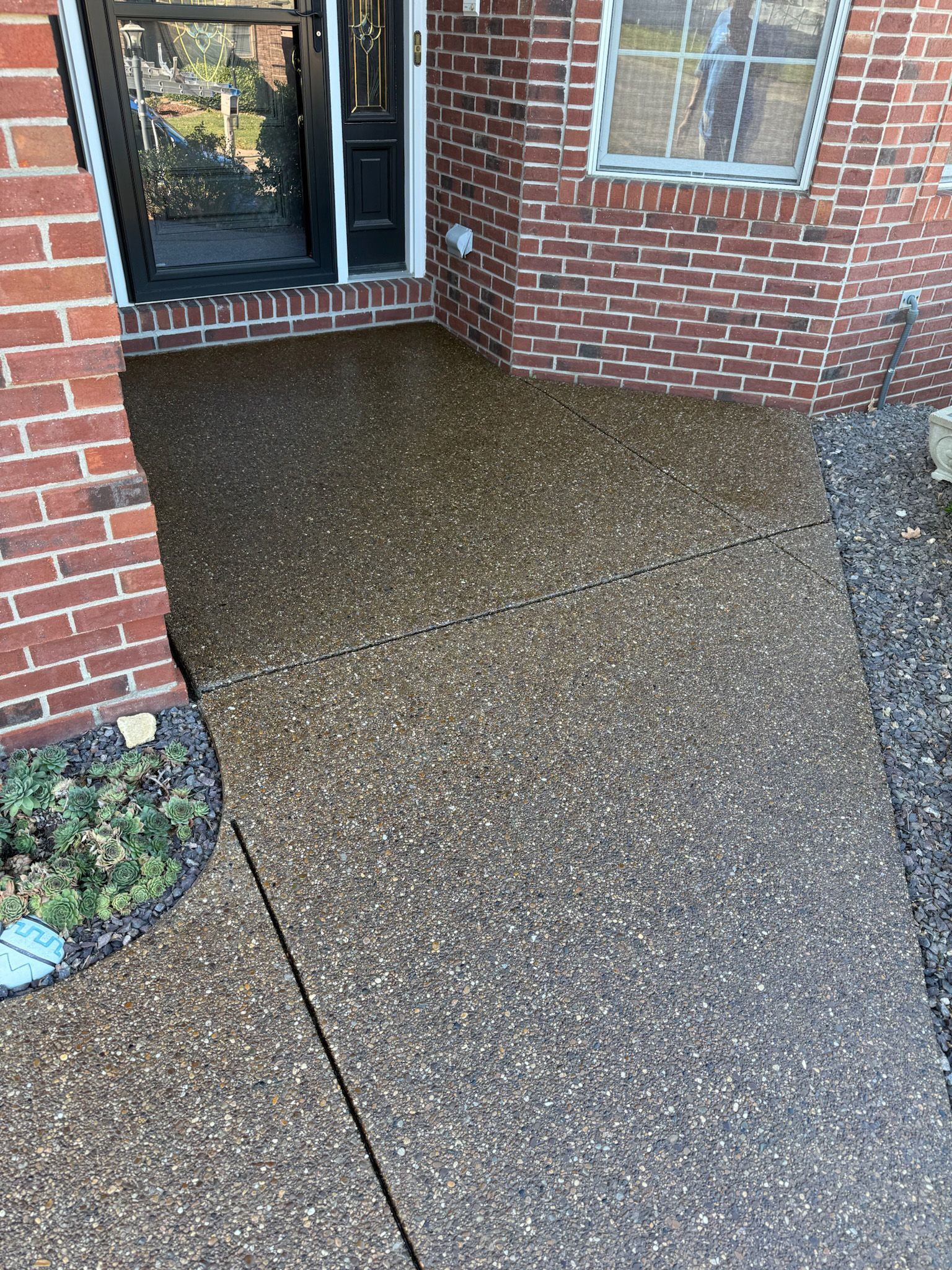 Porch with aggregate concrete. Red brick walls surround a doorway.